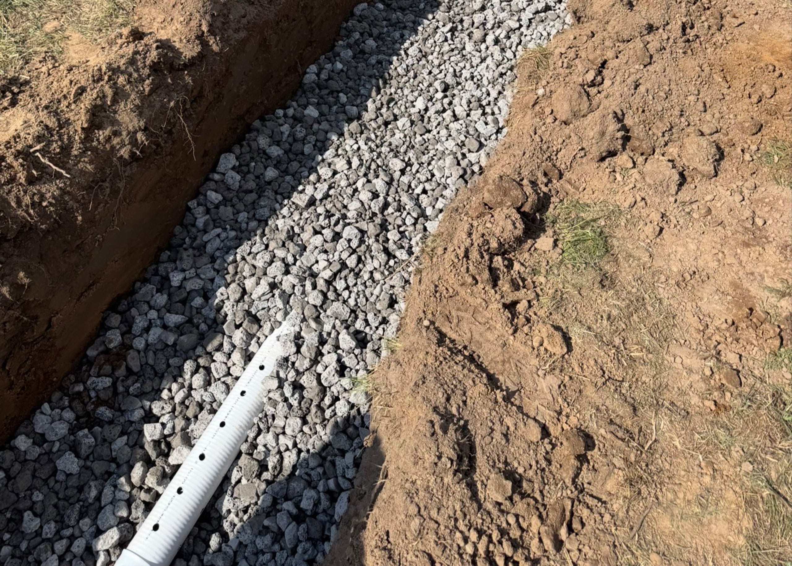 Septic system drain field installation with gravel trench and perforated pipe for proper wastewater drainage and soil filtration